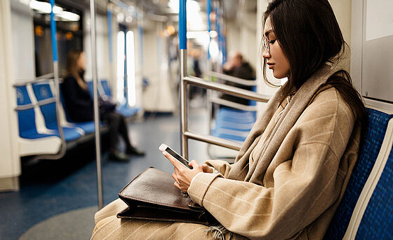 a young woman looks at her mobile phone while sitting in the train